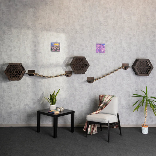 Cat Wall House with Built-in Cat Bridge displayed as modern hexagonal wooden modules connected by sleek bridges, mounted on a textured grey wall above a stylish chair and side table, creating an elegant and functional feline playground.